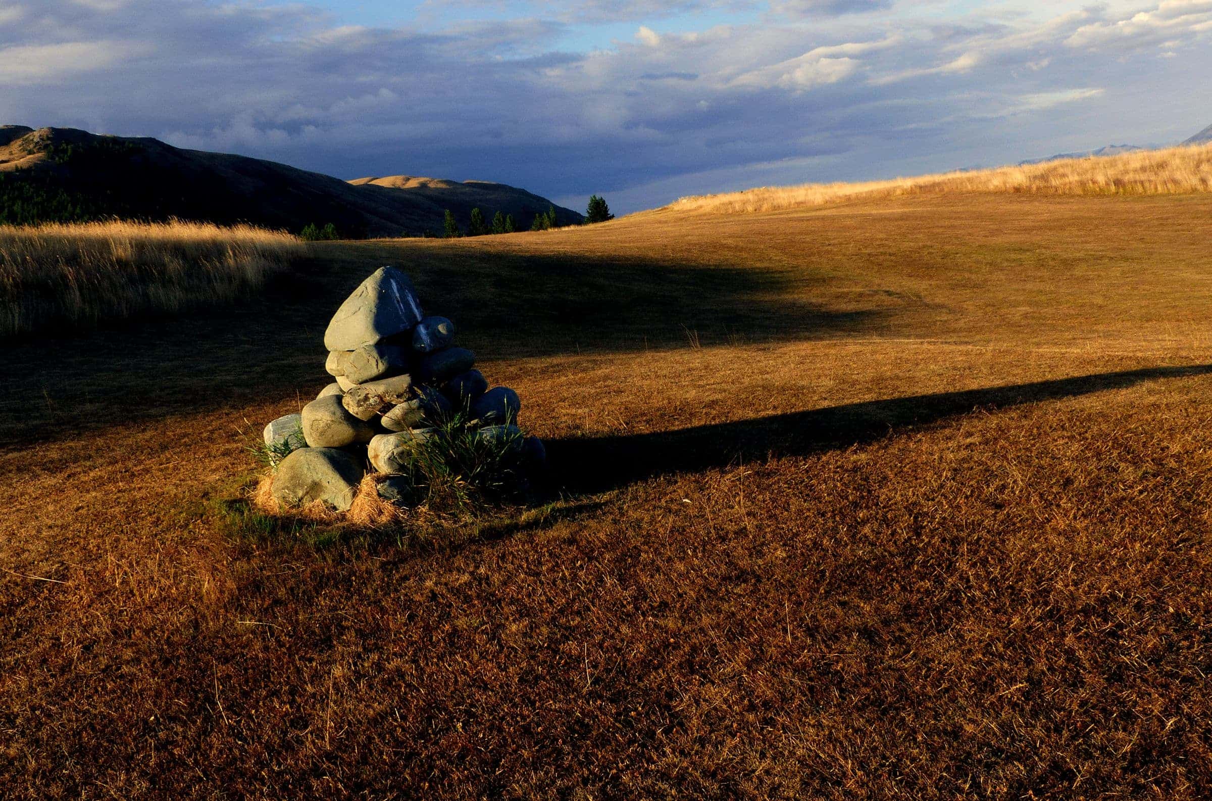 A stone cairn on a golden, sun-raked hillside under a deep-blue sky
